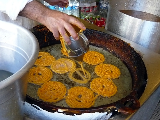 man swirling sweet dough spirals (Zlebia) in a pan of hot oil