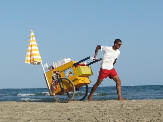 icecream seller pulling a cart along a beach with the sea in the background