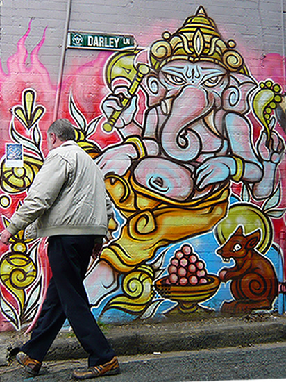 man walks in front of  graffiti of Ganesh the elephant headed god