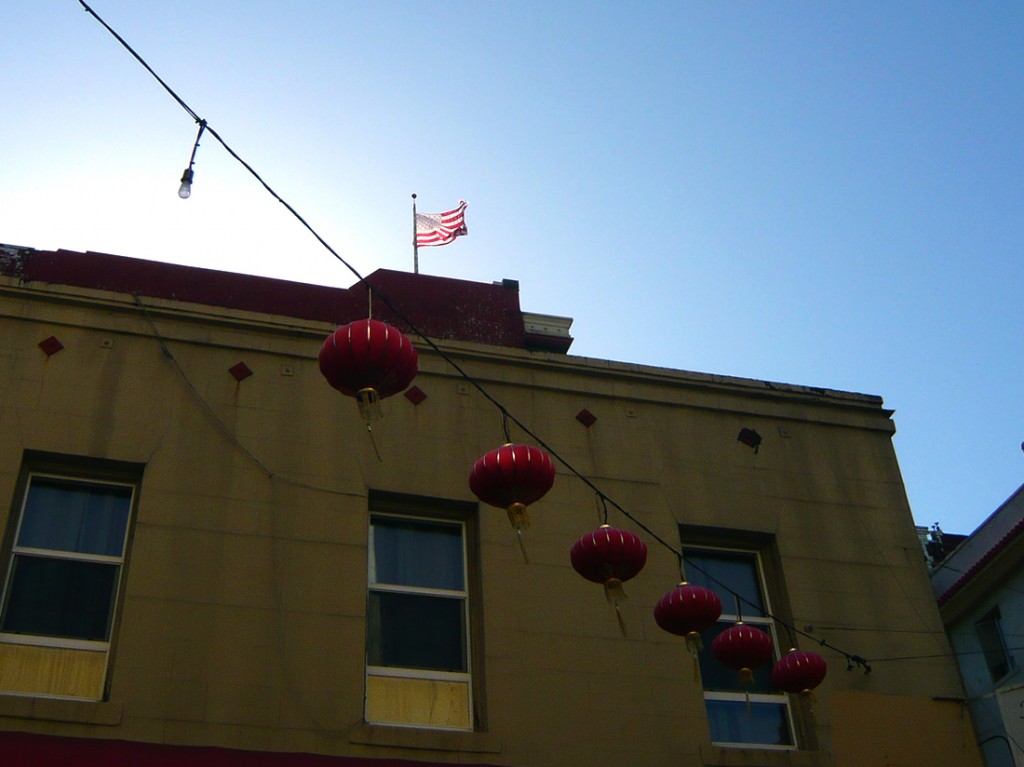 Chinese lanterns hanging in San Francisco's china town, American flag (stars and stripes) flying against a blue sky in the background