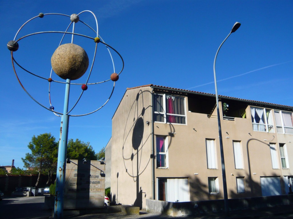 large sculpture of an "orrery" or planetary model (representing spheres in orbit) casting a shadow on the side of a house