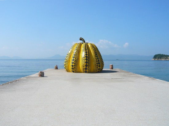 view of a large fiberglass, yellow pumpkin covered in with back dots on a cement pier