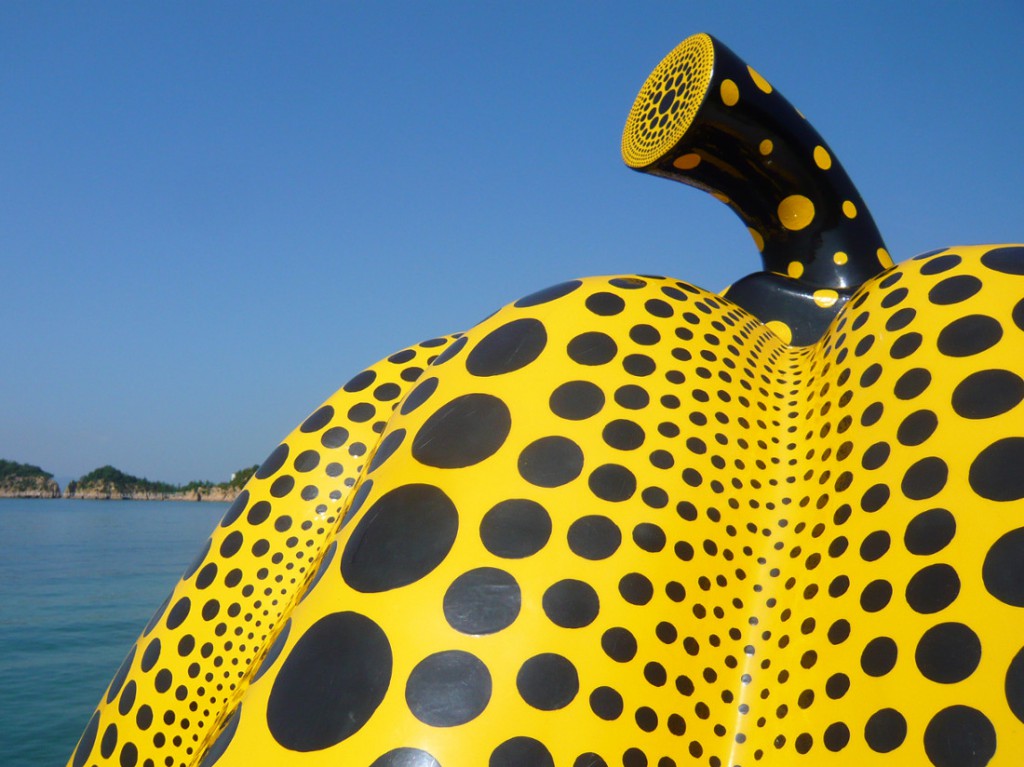 sculputure of large yellow pumking with back dots against a blue sky