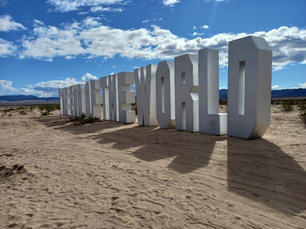 Large upright silver Hollywood-sign-style letters spelling out THE END OF THE WORLD in a desert landscape. 